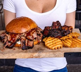 Guest holding a board with the Oh Daddy Burger, ribs and waffle fries