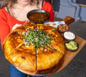 Guest holding the Brisket Birria Quesadilla with dipping sauces