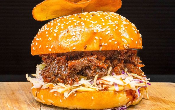 Vrisket burger topped with coleslaw and a crispy chip garnish