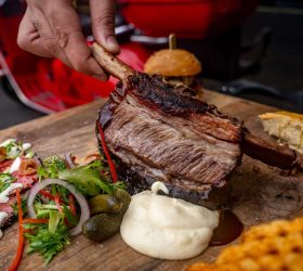 Wagyu beef rib lifted from a board with dips and waffle fries