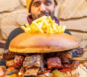 Guest holding the Almighty Burger topped with fries and a rib bone