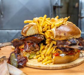 Almighty Burger halves piled with fries and rib bones on a board