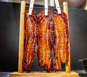 Candied bacon strips hanging from pegs on a rack