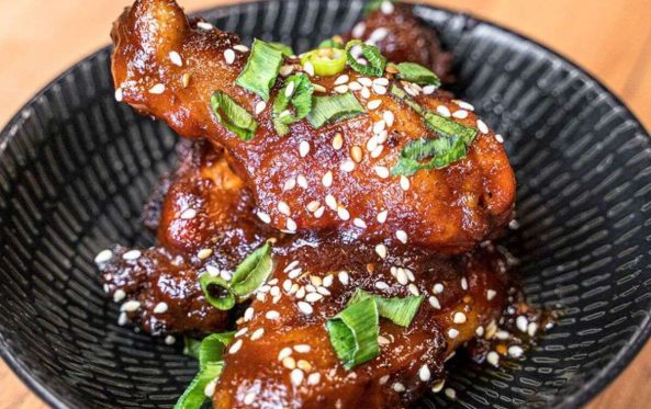 Glazed chicken drumsticks with sesame seeds and herbs in a bowl