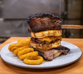 Beefy Mega Stack tower with a brisket rib, onion rings and fries on a plate