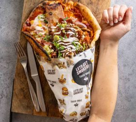 Guest holding the folded Pizzalaki topped with sauce and melted cheese