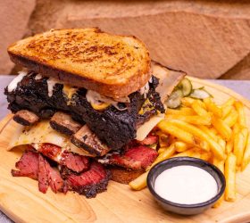 Reuben on Steroids sandwich with fries and dipping sauce on a board