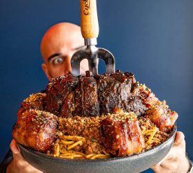 Guest holding the Ultimate Smoked Spag Bol topped with a whole smoked hock