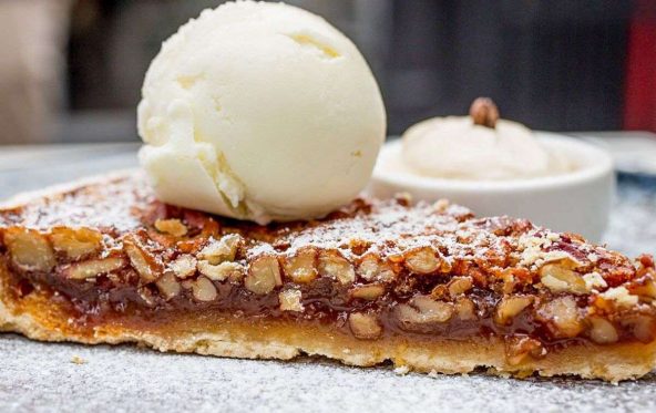 Slice of pecan tart dusted with icing sugar, topped with two scoops of ice cream