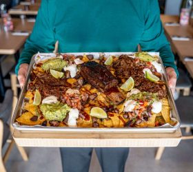 Triple beef nachos on a tray with guacamole and lime, being carried