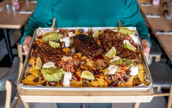 Triple beef nachos on a tray with guacamole and lime, being carried