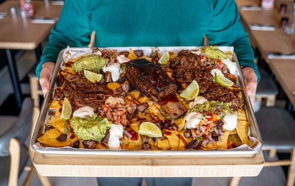 Triple beef nachos on a tray with guacamole and lime, being carried